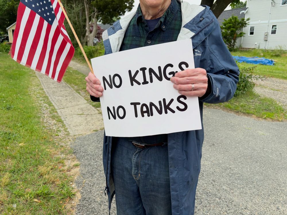A man holding an American flag and a sign reading "No Kings No Tanks"