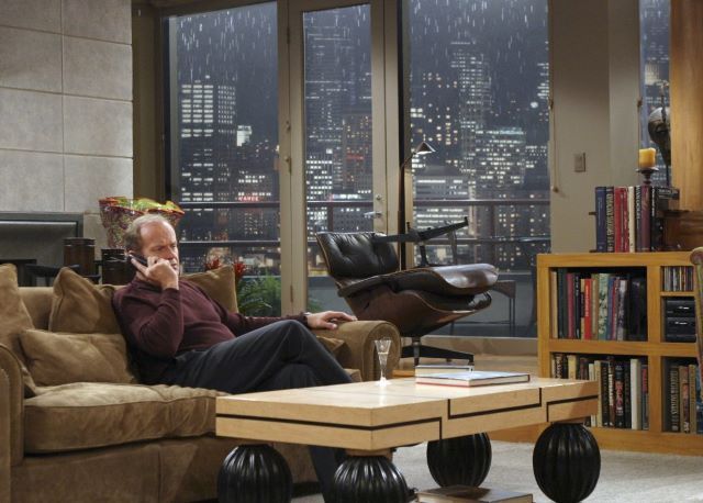 Picture of Frasier's crane apartment. Frasier is seen sitting on the couch talking on the phone.