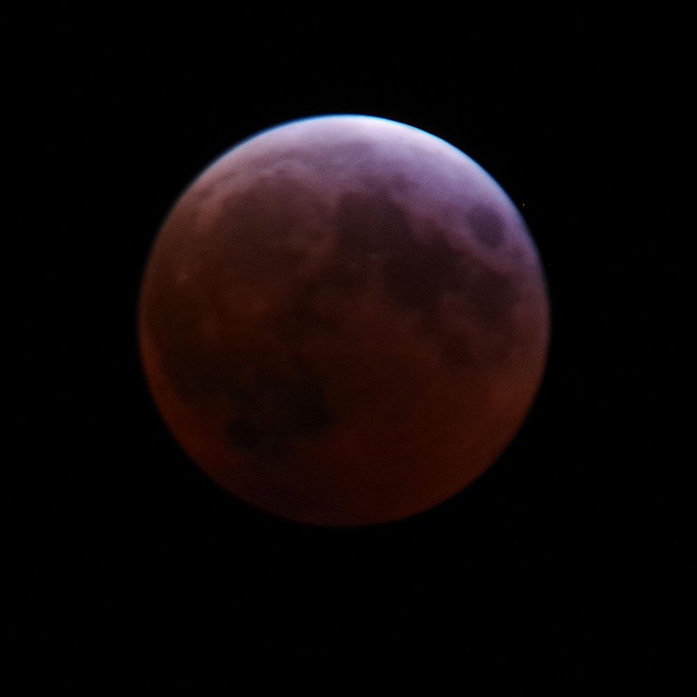 A photograph of the moon in almost total eclipse, tinged red by the earth's shadow.