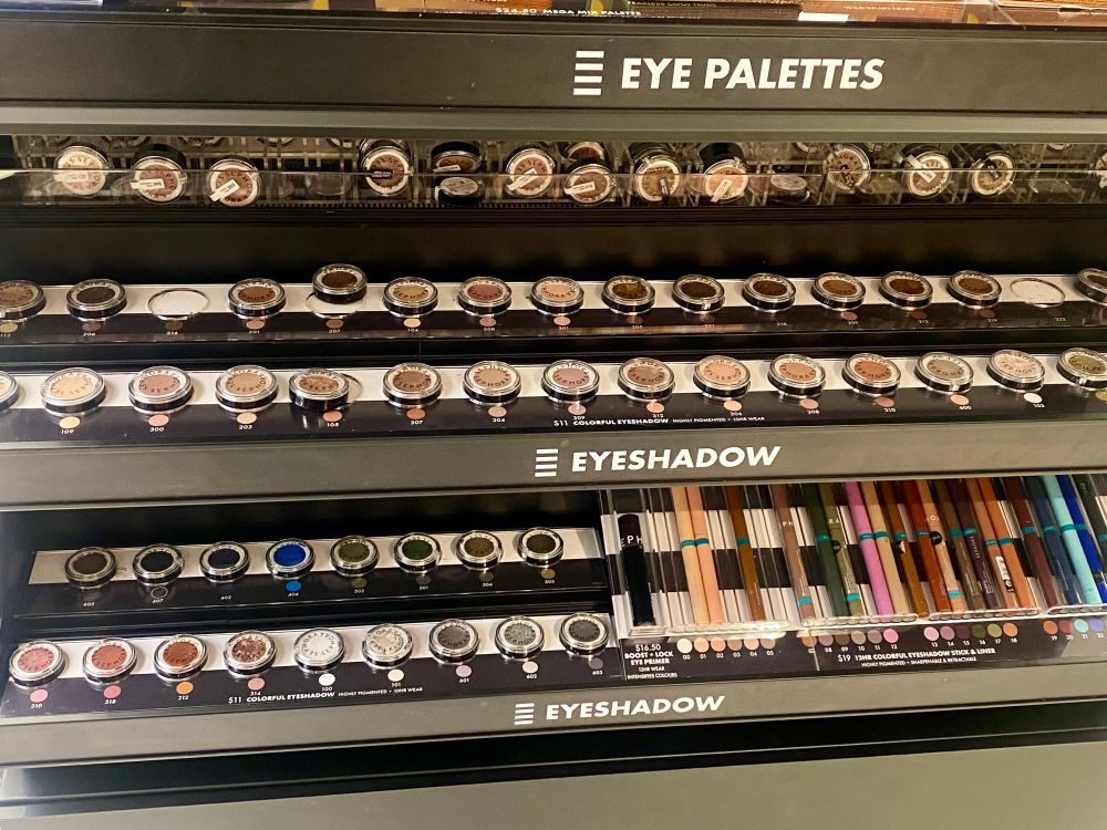 A display of Sephora eyeshadows. All of them are neutral tones except for one (1) dark blue eyeshadow and a few blue eyeliner pencils. 