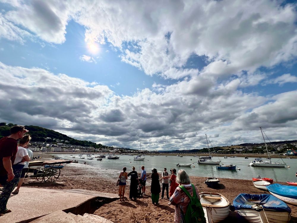 A group of people stand on the shore of an estuary waiting for the ferry boat to take the to the other side.