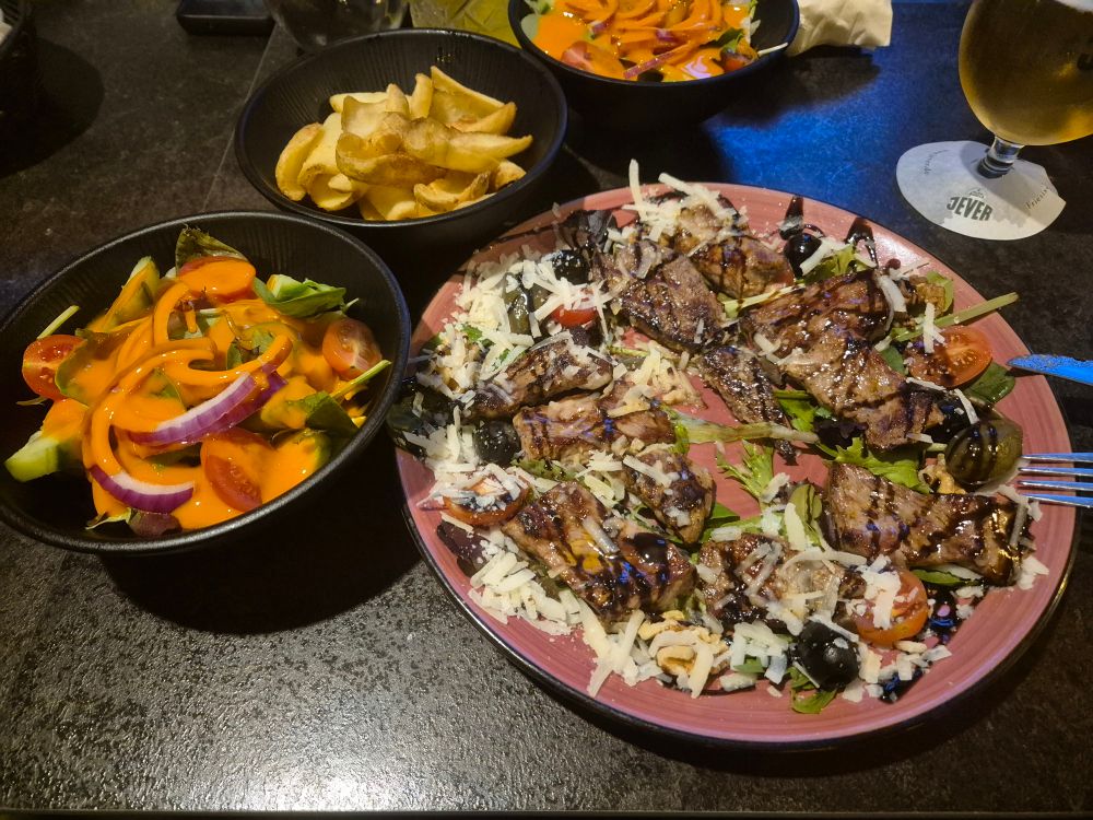 Rinderfilet in Streifen geschnitten, auf einem Rucola Parmesan Bett, angerichtet mit Balsamico, dazu noch Verteilt, Oliven, Feigen und Walnüsse.

Links daneben ein Beilagensalat, dahinter von Restaurant selbst gemachten Pommes.