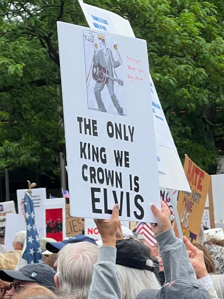 Hands holding a sign at a protest that says, “THE ONLY KING WE CROWN IS ELVIS” under a picture of the King himself.