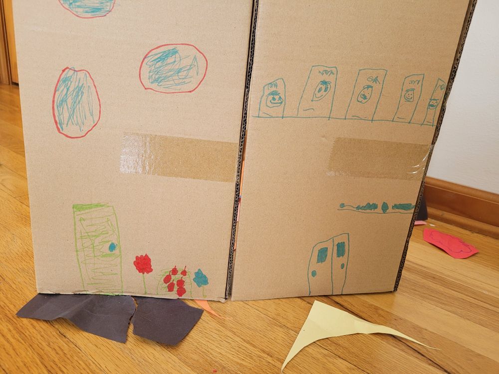 A child's cardboard box craft. On the boxes are drawings of houses. 