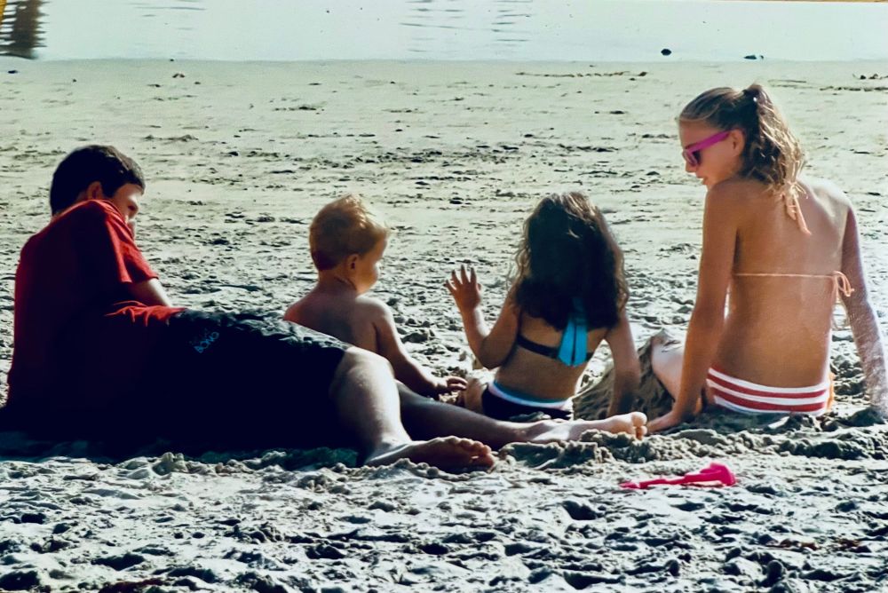 Daughter and animated niece chatting on beach while son and nephew listen 