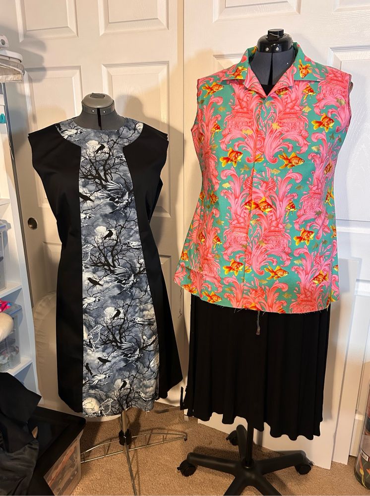 A black dress with crow detail and an aqua and pink shirt with goldfish, both on dress forms.