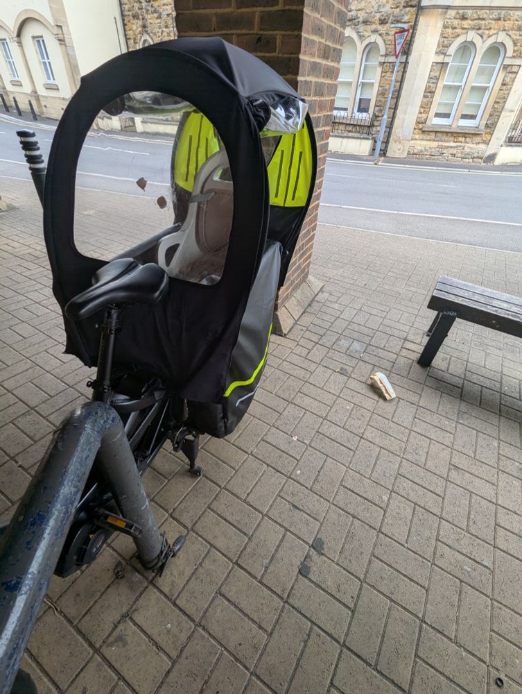Cargo bike struggling to fit in cycle space at a supermarket due to benches and a pillar. 