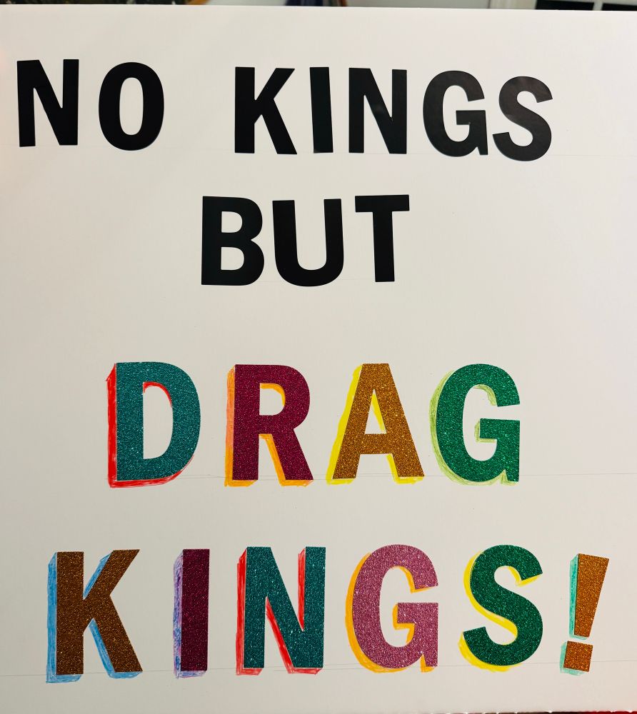 Protest sign reading NO KINGS BUT DRAG KINGS! — the top part is in black block letters, the bottom part is in larger rainbow glitter block letters