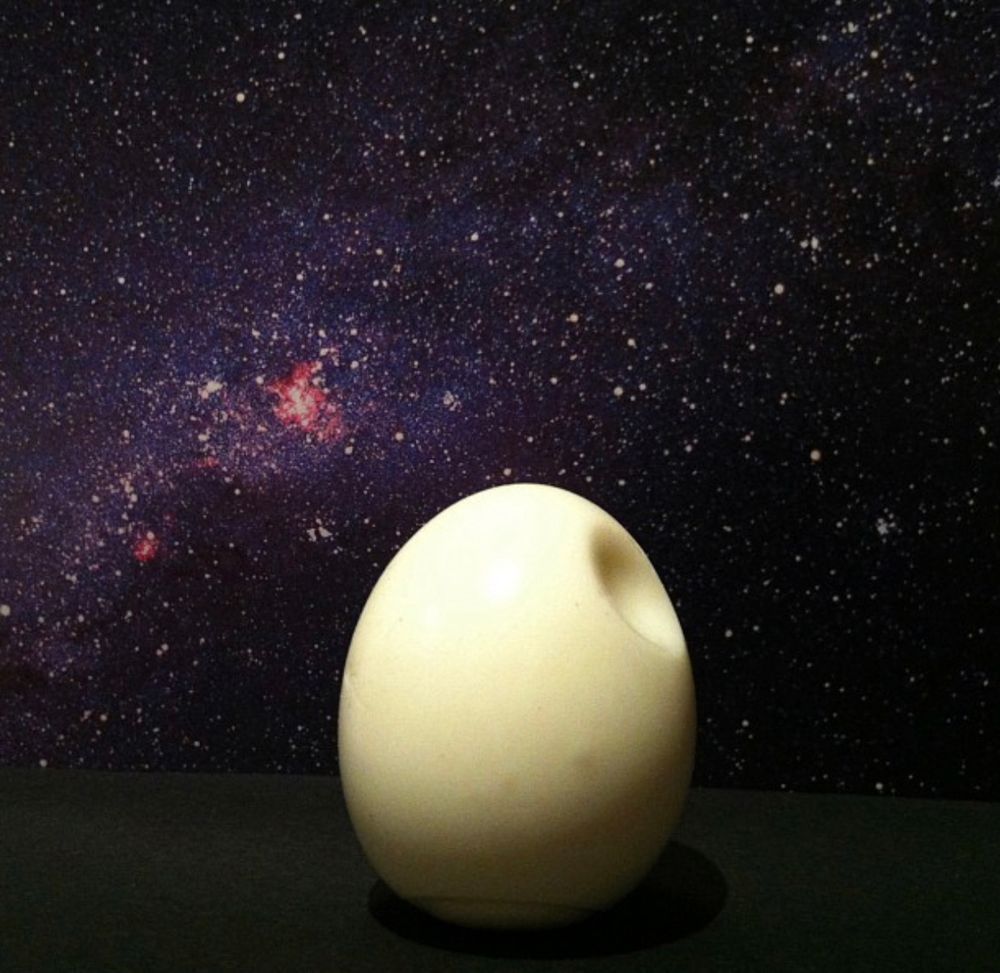 A boiled egg with a circular dent hear the top. It is  photographed in front of an open book which has a picture of a star field. The overall effect is to make the egg look like the Death Star from the movie ‘Uh-Oh, Here Comes The Death Star’.