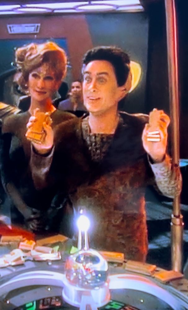 An undisclosed version of the Vorta Weyoun standing at Quark’s dabo table. He looks happily surprised holding up two handfuls of gold-pressed latinum.