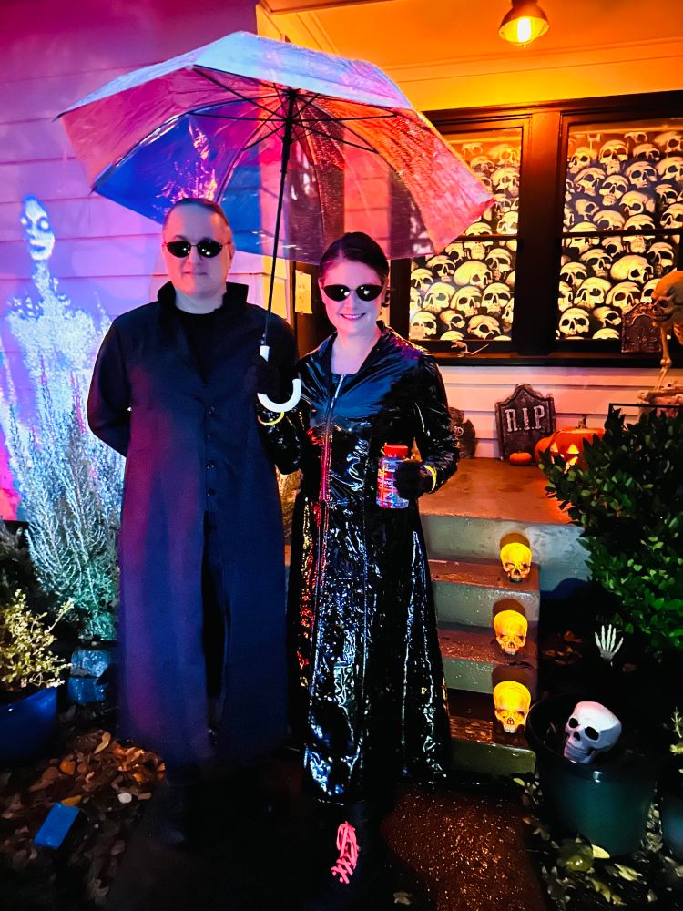 Couples Halloween costume Neo & Trinity from the matrix in front of house decorated for Halloween.
