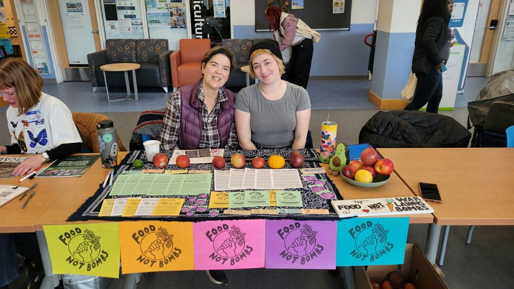 Two people behind a table with Food Not Bombs information.