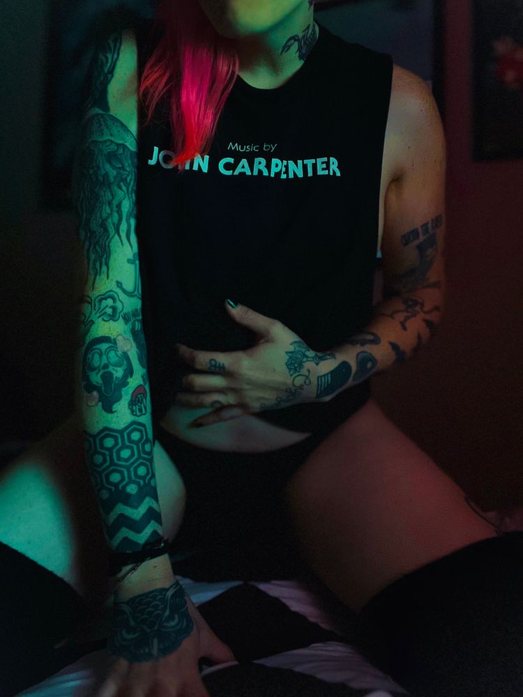 queer tattooed enby with pink hair kneeling in bed wearing thigh highs, undies, and a John carpenter cropped tee