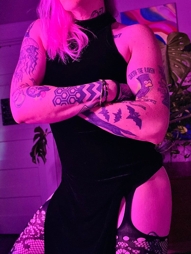 nsfw queer tattooed enby wearing a black dress and garter stockings