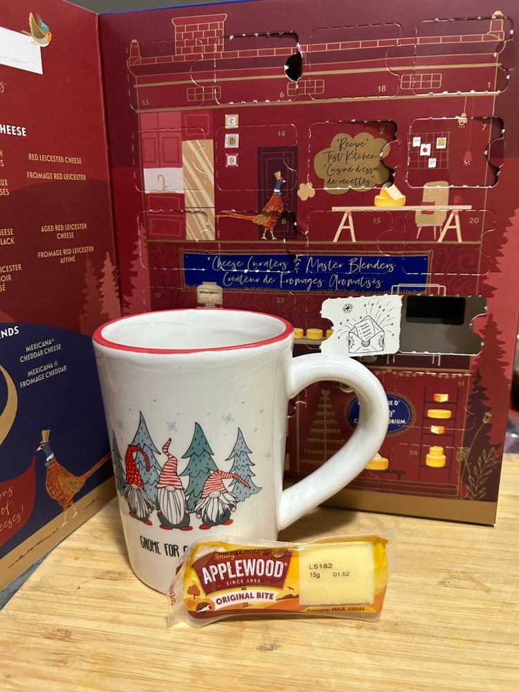 Cheese Advent calendar. Picture behind door is a Christmas card. Applewood smoked cheddar is the small piece of cheese today. The Christmas mug has three gnomes on it and says ‘Gnome for Christmas’