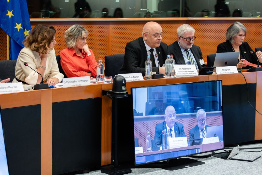 Five of the panel sitting behind a desk, the television screen shows Dr Arafat speaking 