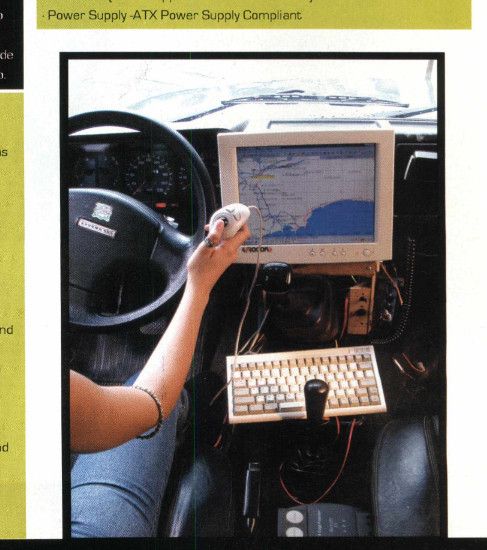 Pessoa dirigindo um carro com um monitor CRT e um teclado instalados no painel, usando um joystick para controlar o sistema. Na tela, há um mapa com rotas, sugerindo uma forma primitiva de navegação automotiva ou GPS improvisado.