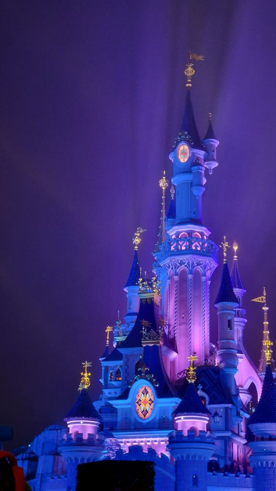 The Sleeping Beauty castle at Disneyland Paris lit up in blue and pink at night
