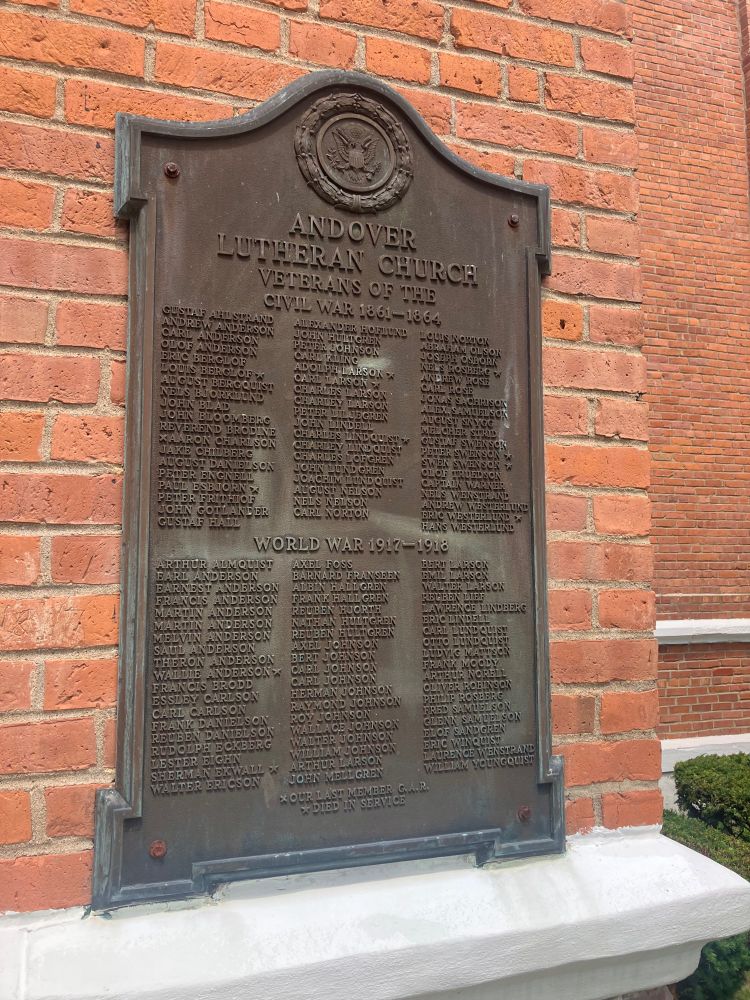 A bronze plaque on a brick wall listing veterans’ names. 