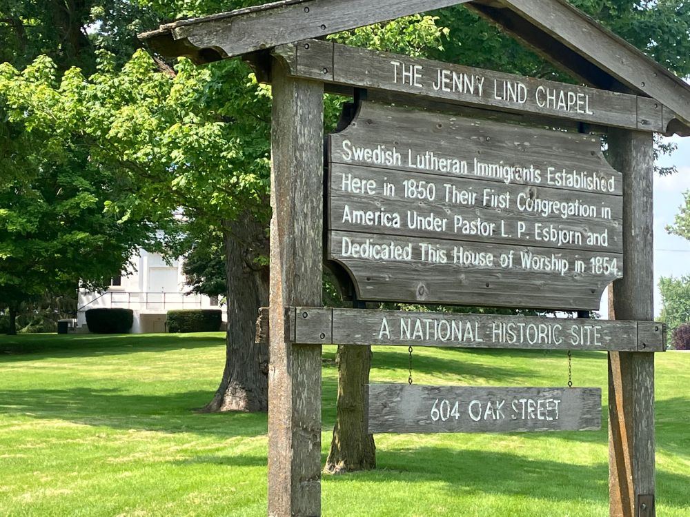 The front of the marker with the chapel behind it. It reads, “THE JENNY LIND CHAPEL: Swedish Lutheran Immigrants Established Here in 1850 Their First Congregation in America Under Pastor L.P. Esbjorn and Dedicated This House of Worship in 1854. 

A NATIONAL HISTORIC LANDMARK 