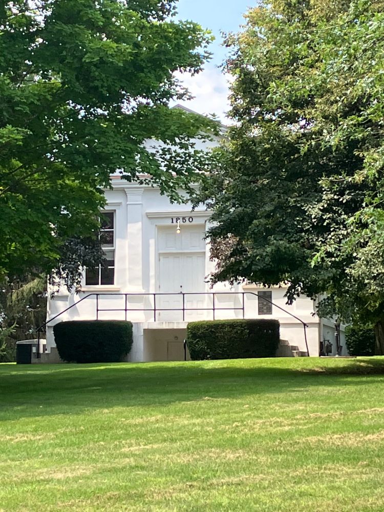 The exterior of the front of the chapel, a white building framed by oak trees. Steps from either side lead up to the front door. 
