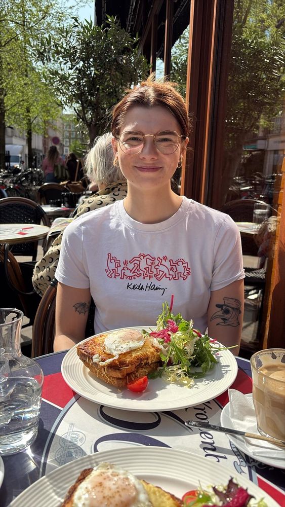 A girl smiling at a restaurant with a croque madame and salad in front of her 