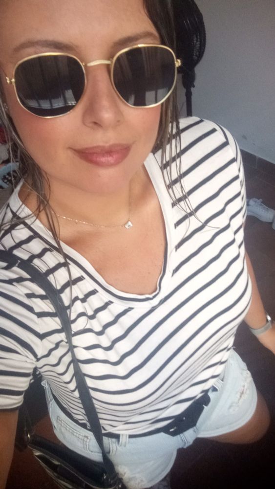 Estou de óculos escuros, uma blusa listrada, short jeans e um cinti preto
 Bolsa pendurada no ombro direito. Vou beber kkkkkkkk
