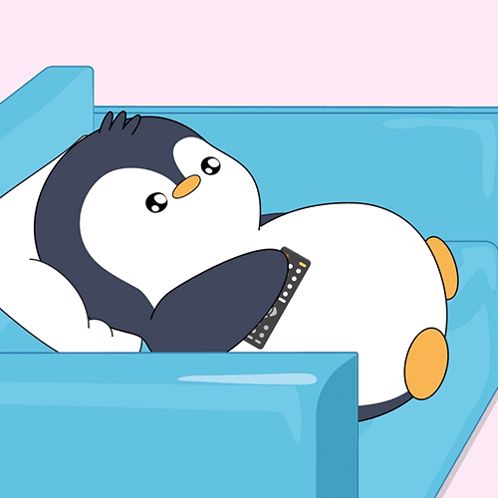 a penguin laying on a blue couch with a remote control