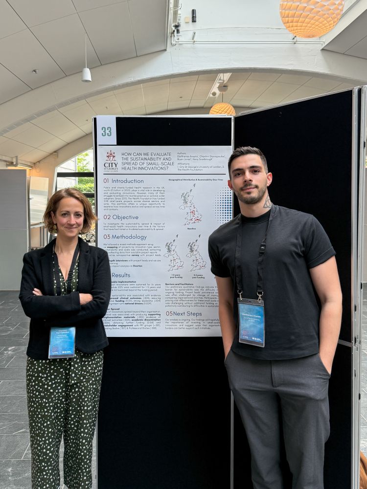 Two people (male and female) standing in front of conference research poster about the evaluation of spread and sustainability of small-scale, funded health innovations in the UK.