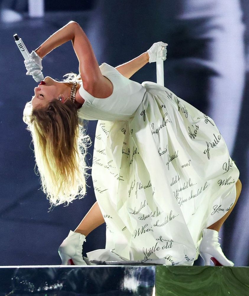 Taylor Swift performs in an ivory dress covered with the words, “Who’s afraid of little old me?” She is bent over backward while singing into the microphone during the rage-filled TTPD set of her world renowned Eras Tour that will soon be ending in Vancouver, Canada.