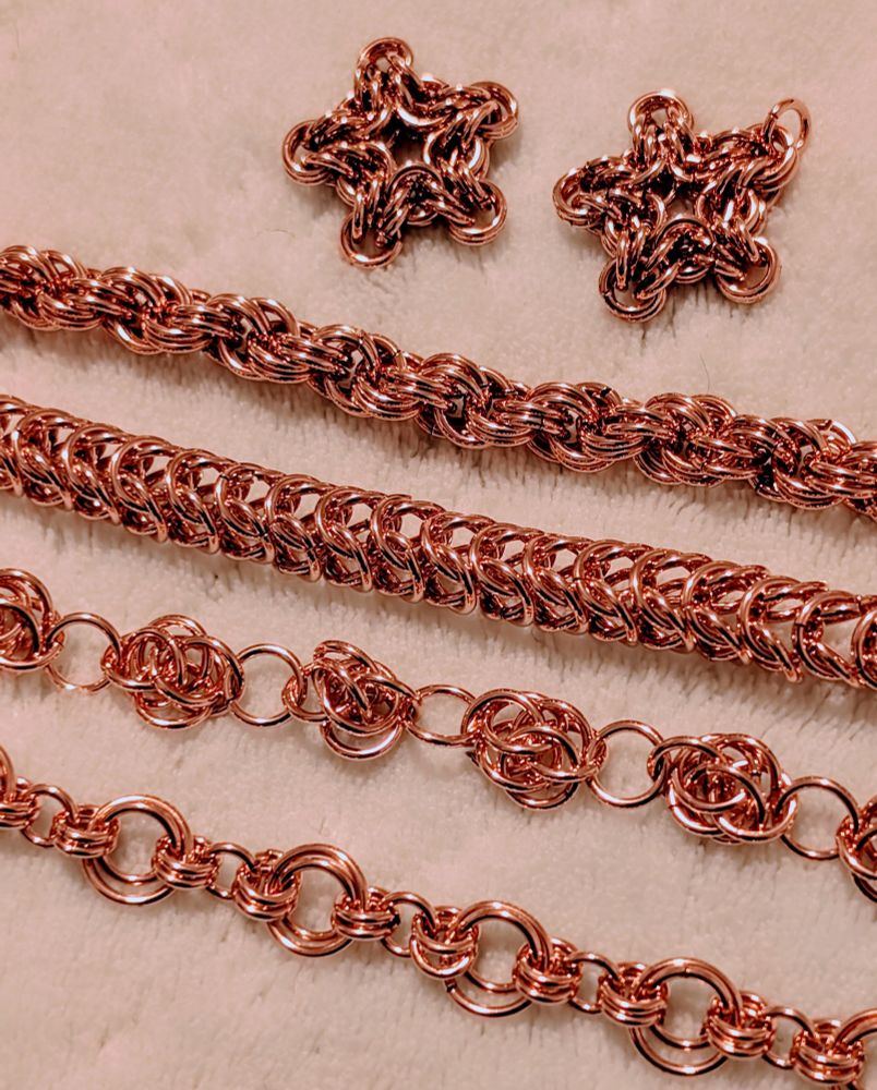 Copper chainmail pendants and chains that have just come out of the tumbler. They are very bright and shiny. Two copper stars made from jump rings, about 3/4 inch in size. One double spiral chain that looks like rope. One box chain. One sweet pea chain. One chain that alternates between large and small rings