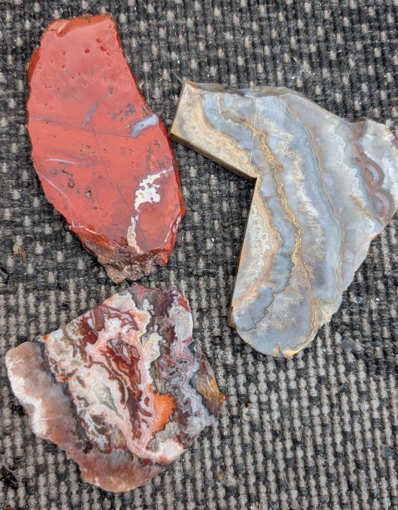 Three rock slabs, one is red jasper, the other two are agate. 