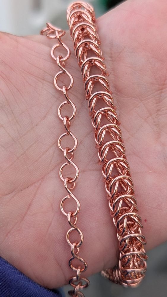 A hand holds two copper chains. One is a bubble chain and the other is a box chain