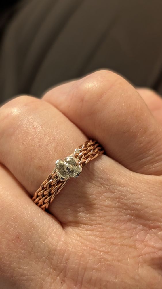 A finger wearing a ring woven from copper wire with a little sterling flower