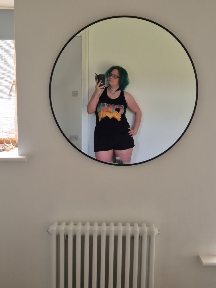 A photo of a green haired guy with their tits away, wearing a shirt with the doom font that reads "CUM" 