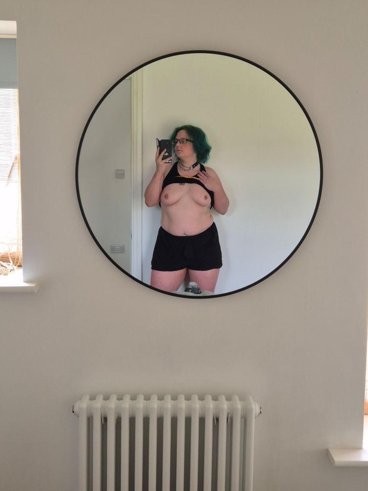 A photo of a green haired guy with their tits out taking a mirror selfie 