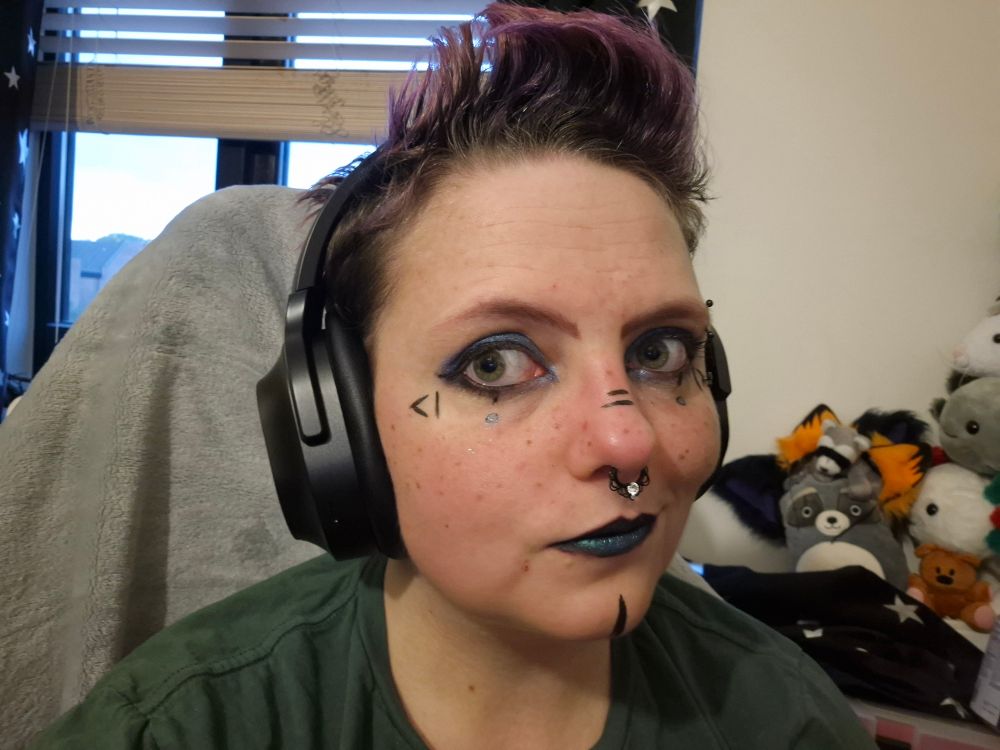 Blue chrome eyeshadow with thick black eyeliner, black nose and chin stripes, blue/black chrome lipstick, vertical lines under the eye with blue outlined dots, on either side of the eyes there are <| |> to replicate the Caravan Palace <| °_° |> robot face