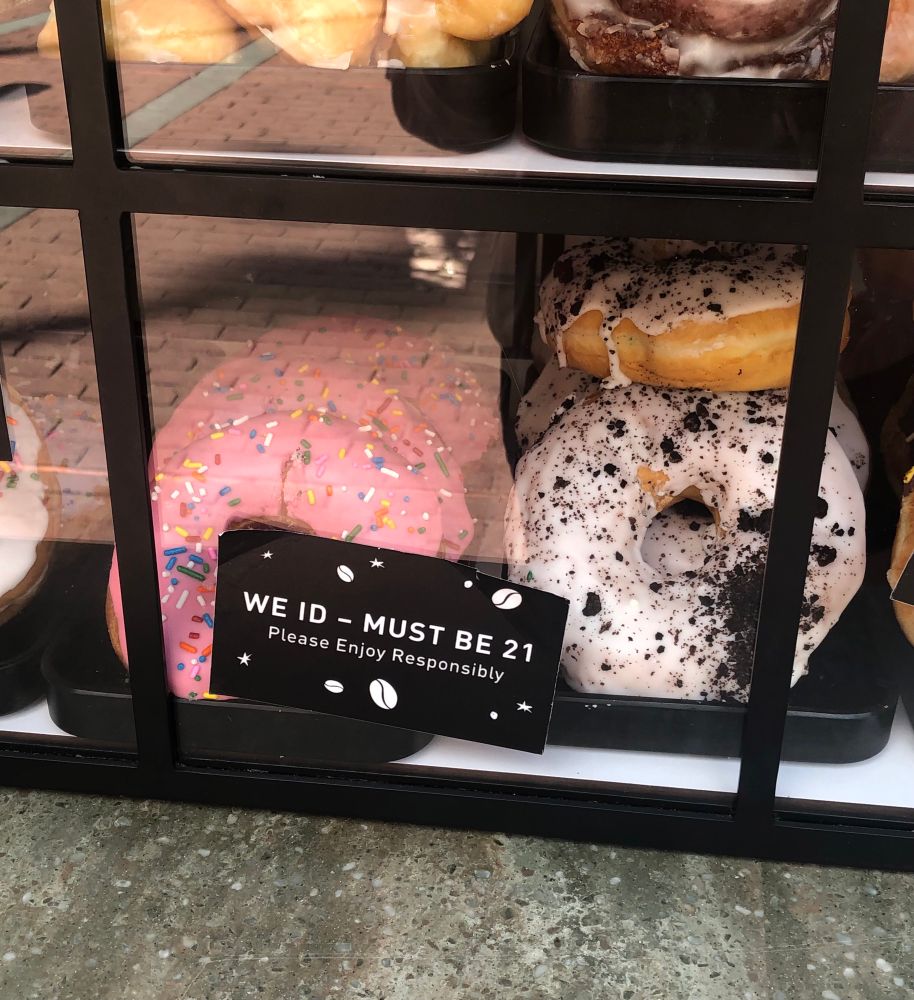 donuts in a cafe case with a sign that says "we id - must be 21 please enjoy responsibly"