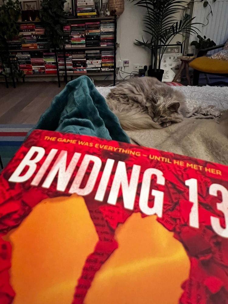 Alberte ligger i en krøll på sofaen, i forgrunnen er boka Binding 13 og bena mine under et teppe.