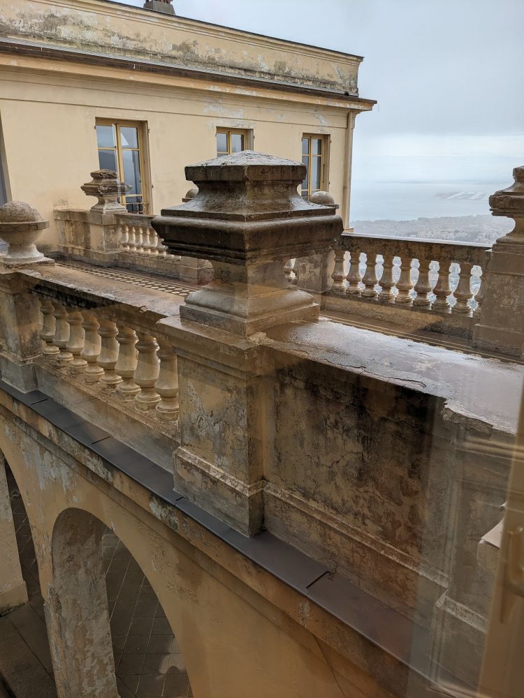 Grand railing-ed walkway of an old building with a cloudy view of a city and bay behind.