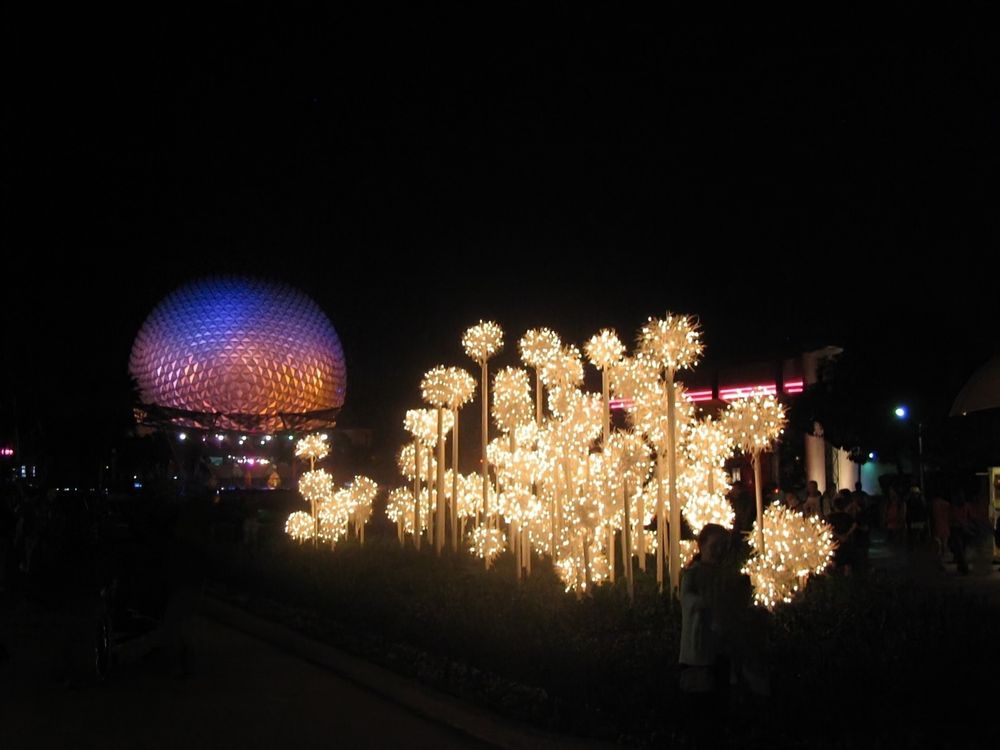 Night picture of illumined Spaceship Earth WDW EPCOT with white lighted decorations in foreground 