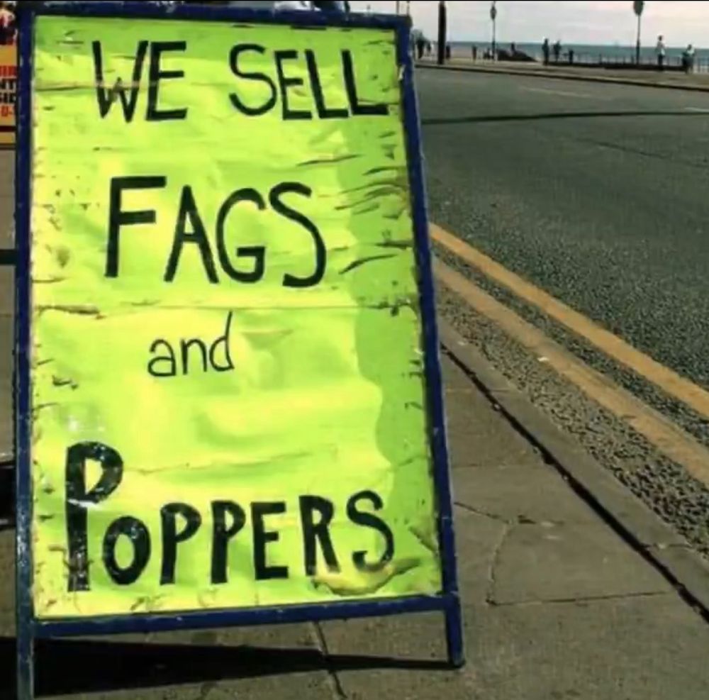 Luminous yellow shop sign which says WE SELL FAGS AND POPPERS 