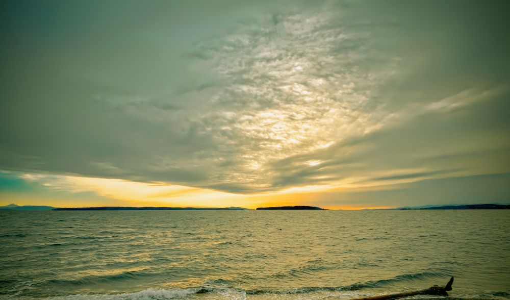 Looking south from a Vancouver Island beach. A large cloud hangs over the foreground and in the distance a brilliant glowing light.