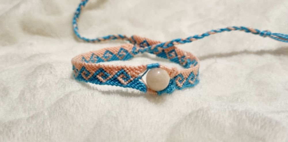 Friendship bracelet arranged in circle.
Wave pattern in blue and pick colors with aquamarin-morganit gemstone in the middle.