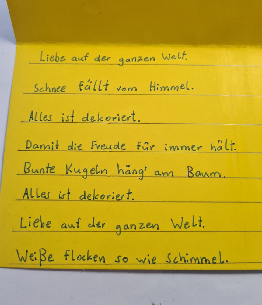 Kinderkarte mit dem Text: Liebe auf der ganzen Welt. Schnee fällt vom Himmel. Alles ist dekoriert. Damit die Freude für immer hält. Bunte Kugeln häng am Baum. Alles ist dekoriert. Liebe auf der ganzen Welt. Weiße Flocken so wie Schimmel.