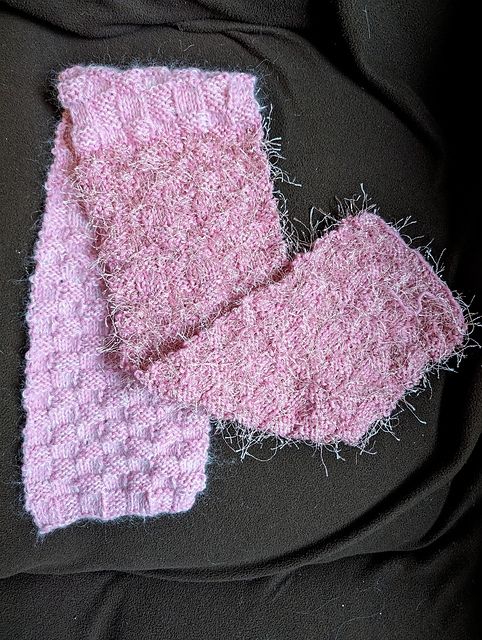 Princess Sparkle Scarf by Gina House is a pink scarf in a basket weave knit pattern that lies on a dark fabric background.