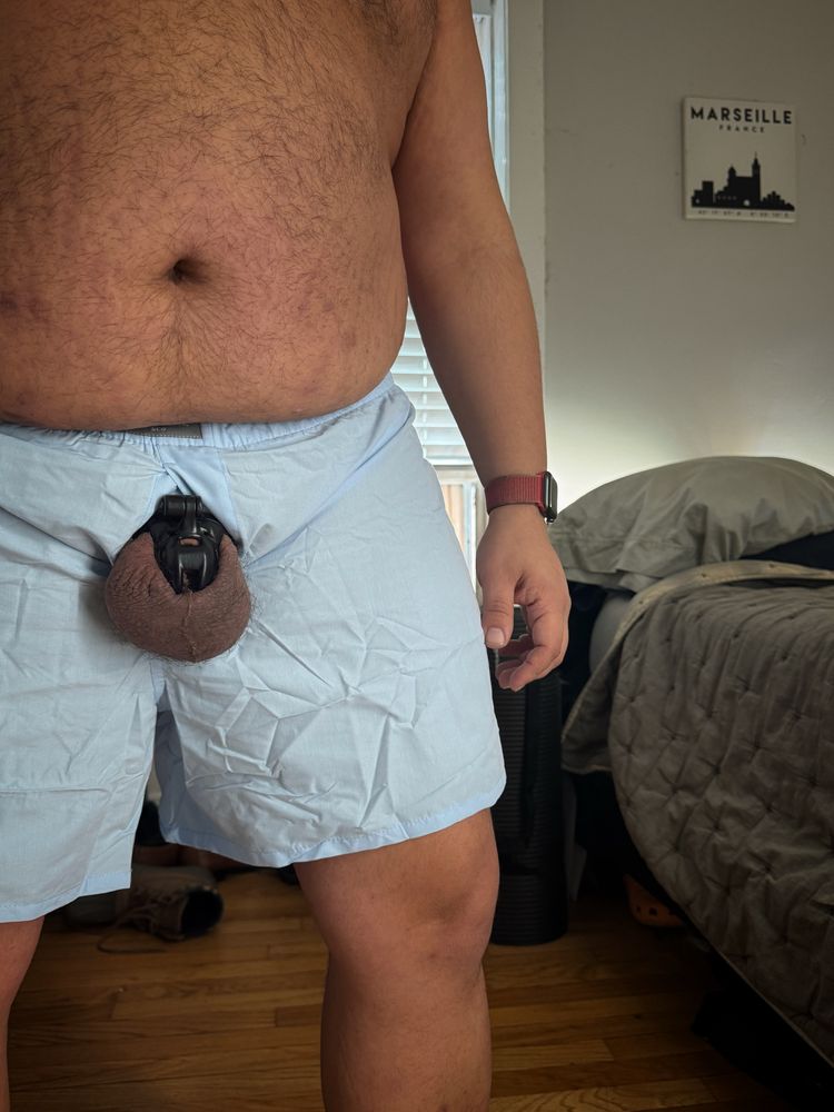 Off center photo of me from mid-chest down to mid-calf. I’m wearing blue boxers and my caged nub and balls are pulled out of the fly