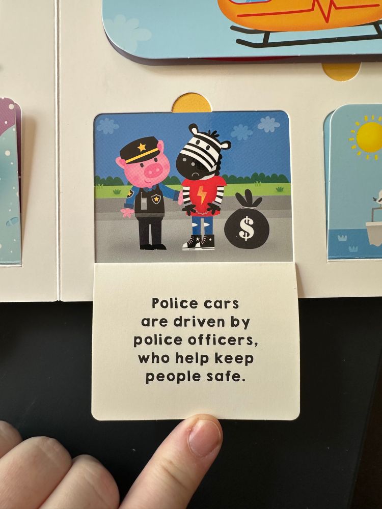 A small flap in a children’s board book. It’s held open, showing a pig as a police officer arresting a zebra with a big bag with a dollar sign on it. The text reads, “Police cars are driven by police officers, who help keep people safe.”
