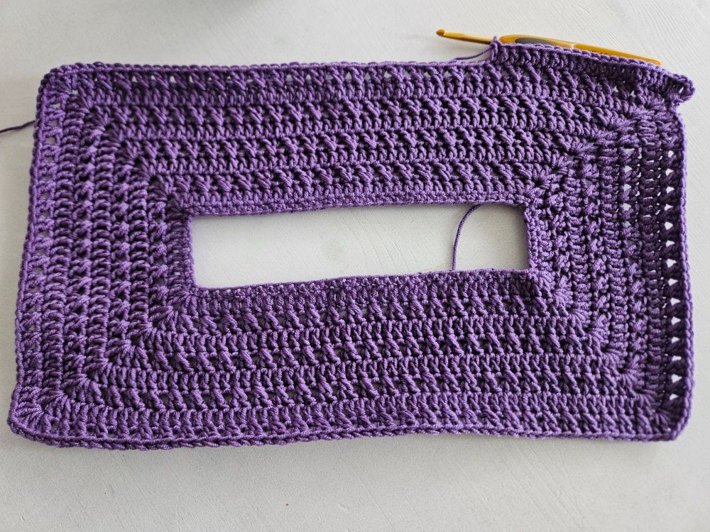 Ein angefangenes lilafarbenes Häkelstück auf weißem Untergrund. 