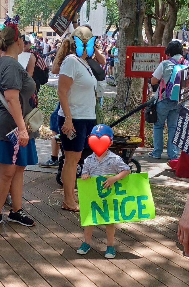 Picture of a little boy around 4 years old holding a sign that says "BE NICE" at the No Kings protest.